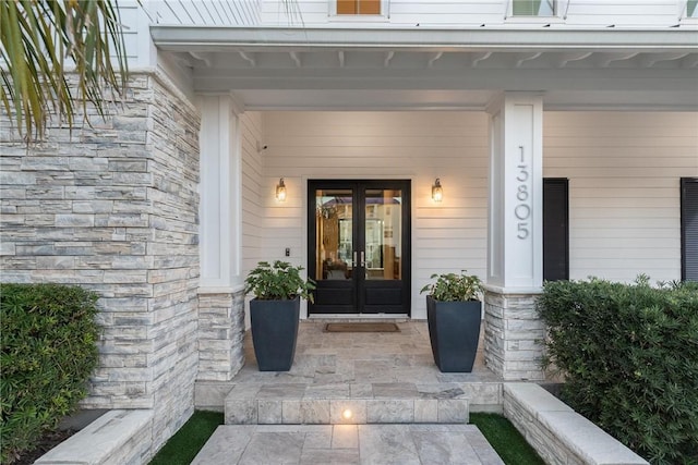 doorway to property with stone siding, covered porch, and french doors