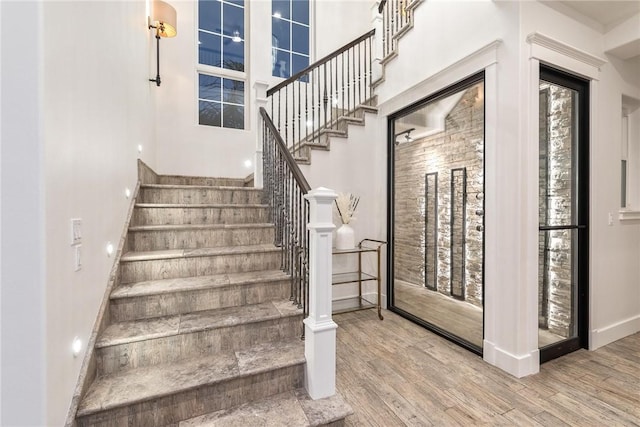 staircase featuring baseboards, wood finished floors, and a towering ceiling