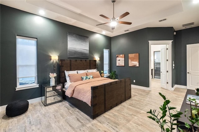 bedroom with baseboards, a raised ceiling, light wood-style floors, and visible vents