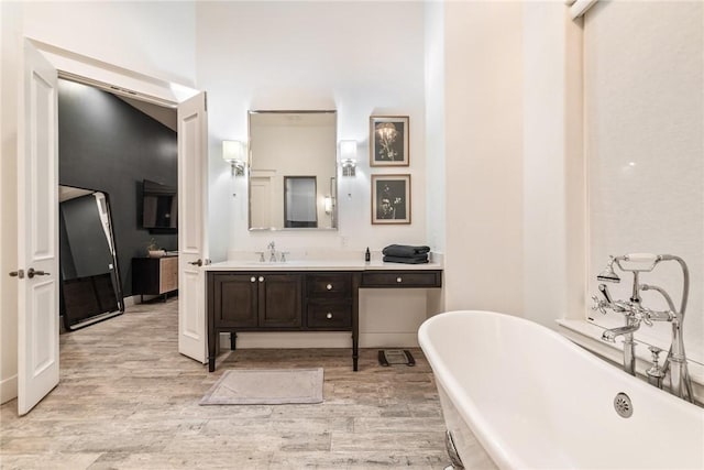 bathroom featuring vanity, a freestanding tub, wood finished floors, and baseboards