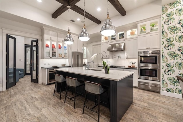 kitchen with a sink, light wood-style floors, appliances with stainless steel finishes, under cabinet range hood, and a warming drawer