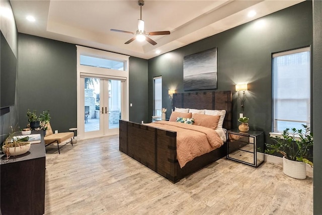 bedroom with access to exterior, baseboards, light wood-style flooring, french doors, and a raised ceiling