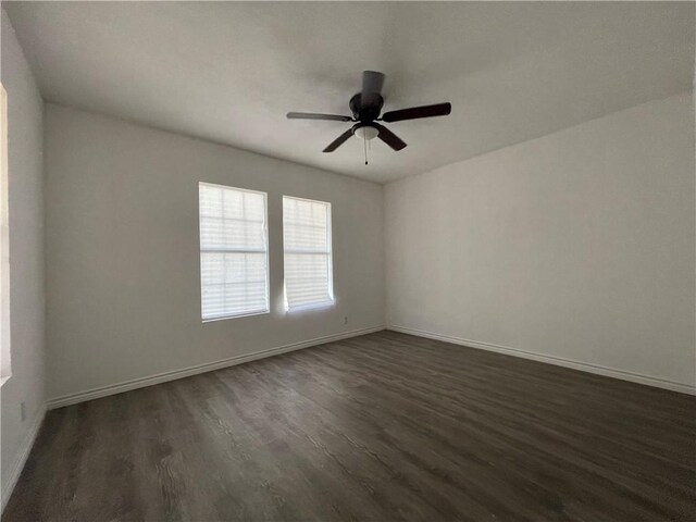 spare room featuring baseboards, dark wood-style floors, and a ceiling fan