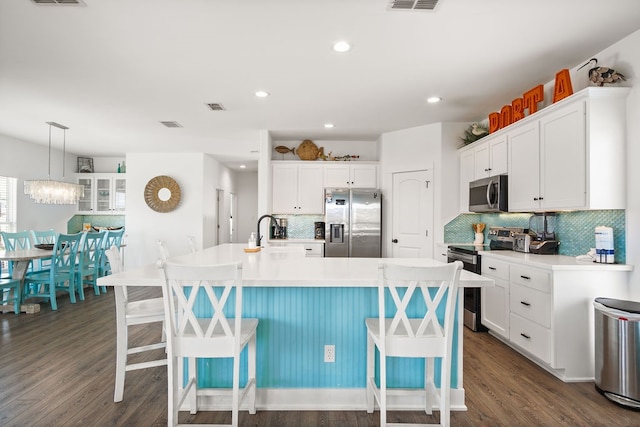 kitchen with a kitchen island with sink, dark hardwood / wood-style floors, a breakfast bar, and appliances with stainless steel finishes