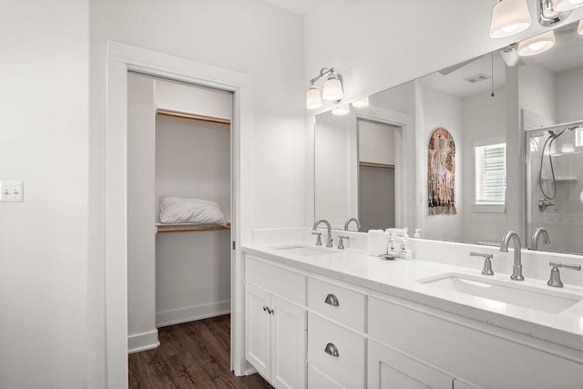 bathroom featuring a spacious closet, a stall shower, wood finished floors, double vanity, and baseboards