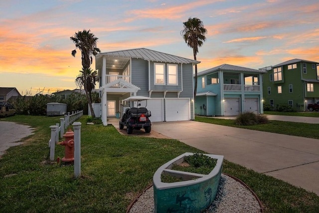 view of front of house with an attached garage, concrete driveway, a front lawn, a balcony, and metal roof