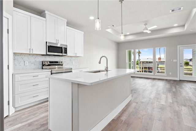 15501 Cruiser St Unit A, Corpus Christi, TX 78418 - kitchen with appliances with stainless steel finishes, a tray ceiling, light wood-type flooring, backsplash, and an island with sink
