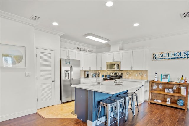 kitchen with crown molding, a kitchen island with sink, stainless steel appliances, a kitchen breakfast bar, and white cabinets