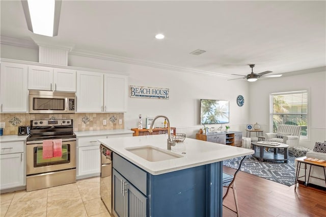 kitchen with sink, white cabinetry, a center island with sink, ornamental molding, and appliances with stainless steel finishes