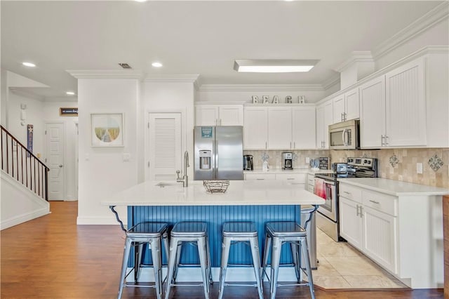 kitchen featuring stainless steel appliances, a center island with sink, white cabinets, and a kitchen breakfast bar