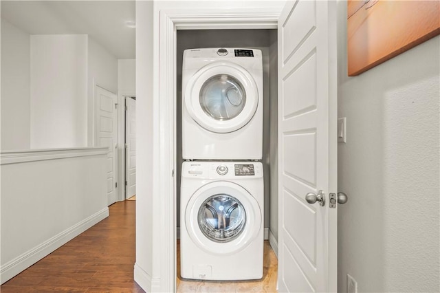 clothes washing area with hardwood / wood-style flooring and stacked washer and clothes dryer