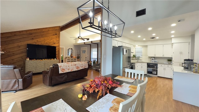 dining space with ceiling fan with notable chandelier, beam ceiling, light wood-type flooring, and high vaulted ceiling