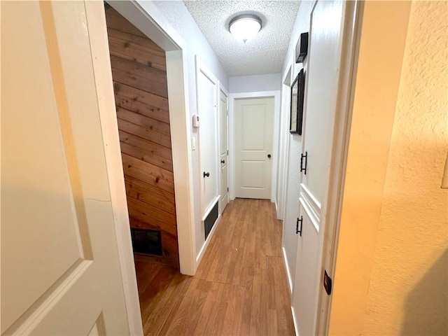 corridor featuring wooden walls, a textured ceiling, and light wood-type flooring