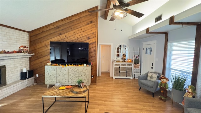 living room with ceiling fan, crown molding, light hardwood / wood-style flooring, high vaulted ceiling, and a fireplace