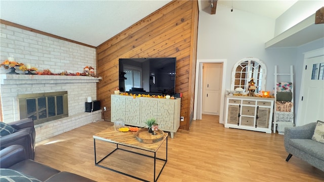 living room featuring a brick fireplace, wooden walls, crown molding, high vaulted ceiling, and light hardwood / wood-style flooring