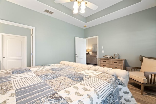 bedroom with visible vents, a ceiling fan, a tray ceiling, and wood finished floors