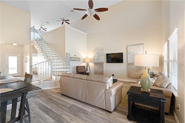 living area featuring a wealth of natural light, a towering ceiling, light wood-style flooring, and a ceiling fan