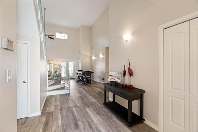 hallway with baseboards, stairs, a high ceiling, and wood finished floors