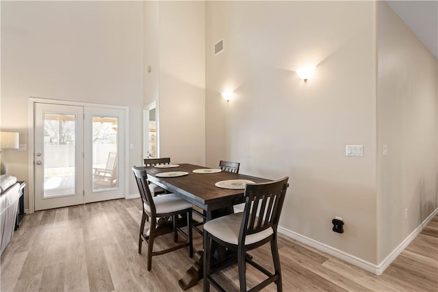 dining space with baseboards, a high ceiling, and light wood-style flooring