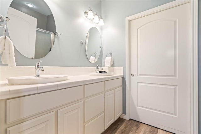 bathroom with double vanity, wood finished floors, a shower with shower door, and a sink