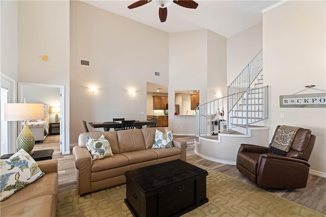 living room with wood finished floors, baseboards, visible vents, ceiling fan, and stairs