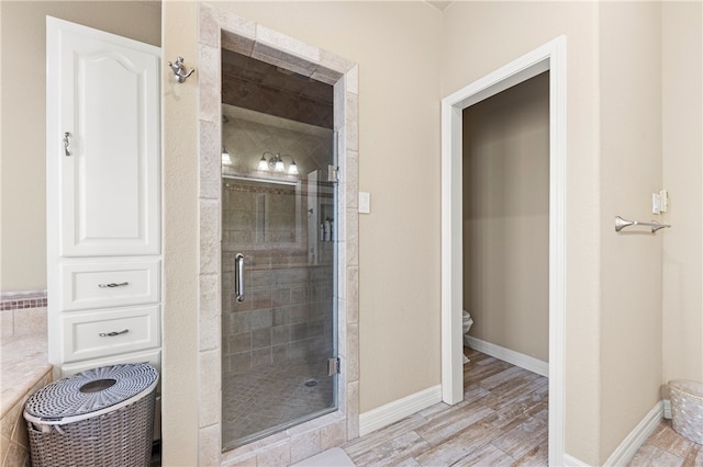 bathroom with hardwood / wood-style floors, a shower with shower door, and toilet