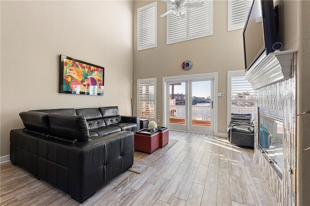 living room with ceiling fan, a towering ceiling, and light hardwood / wood-style flooring