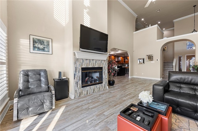 living room featuring ceiling fan, wood-type flooring, ornamental molding, and a high ceiling