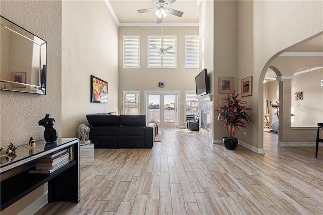 living room featuring ceiling fan, ornamental molding, a towering ceiling, light hardwood / wood-style floors, and decorative columns