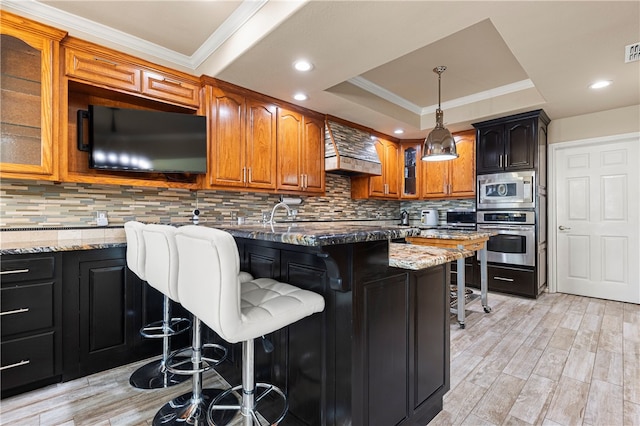 kitchen with light stone countertops, a kitchen breakfast bar, tasteful backsplash, stainless steel appliances, and light hardwood / wood-style floors