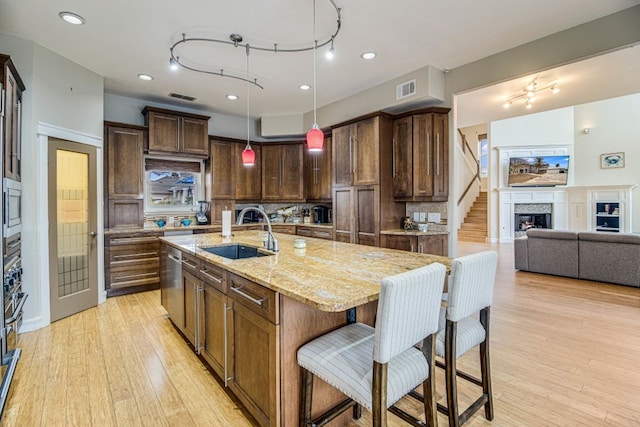 kitchen featuring pendant lighting, tasteful backsplash, sink, a kitchen island with sink, and light stone counters