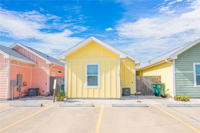 back of house featuring uncovered parking, central air condition unit, board and batten siding, and fence