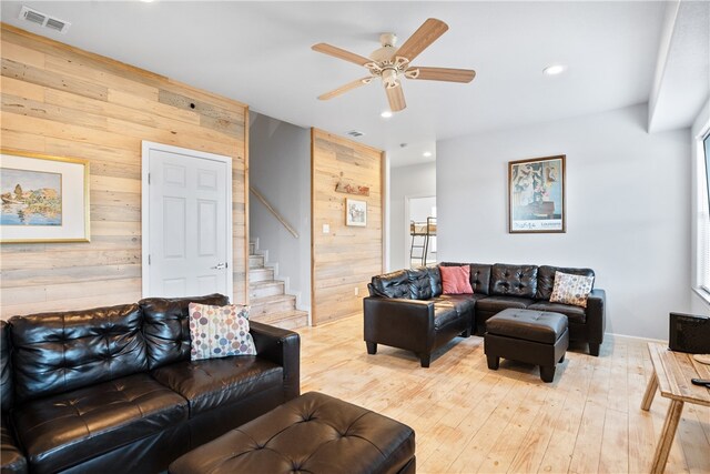 living room featuring light wood-type flooring, wooden walls, and ceiling fan