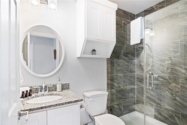 bathroom with a shower with door, vanity, and toilet