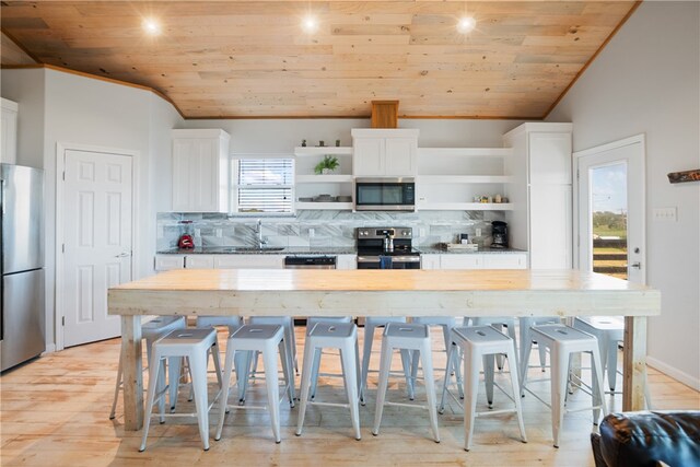 kitchen with a kitchen bar, light hardwood / wood-style floors, lofted ceiling, wooden ceiling, and appliances with stainless steel finishes