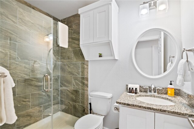 bathroom featuring toilet, vanity, and a shower with shower door