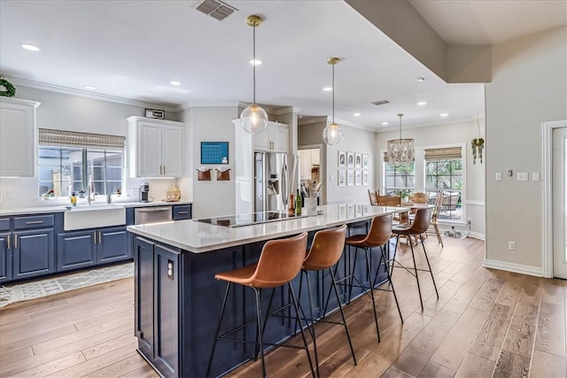 6046 Tarafaya Dr, Corpus Christi, TX 78414 - kitchen featuring blue cabinetry, stainless steel appliances, light wood finished floors, a center island, and ornamental molding