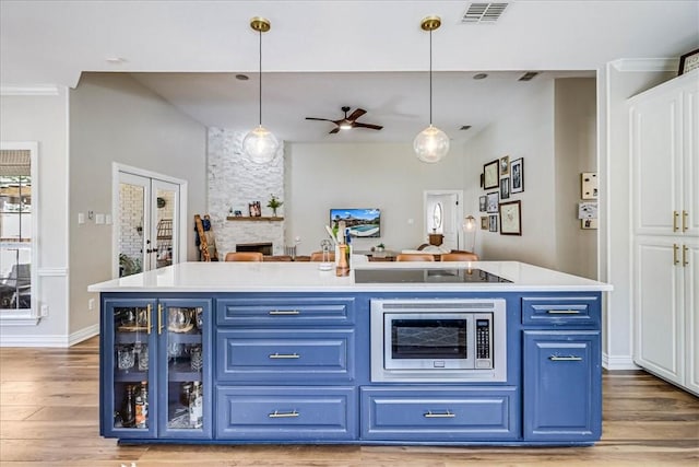 6046 Tarafaya Dr, Corpus Christi, TX 78414 - kitchen with blue cabinetry, stainless steel microwave, wood finished floors, a ceiling fan, and pendant lighting