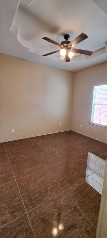 tiled empty room featuring ceiling fan and a tray ceiling