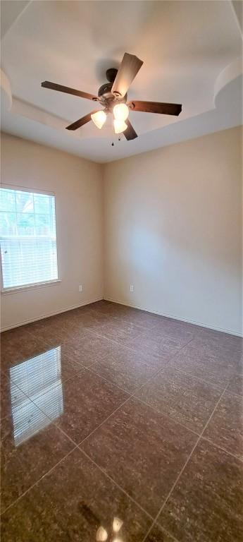 unfurnished room with ceiling fan, a raised ceiling, and dark tile patterned floors