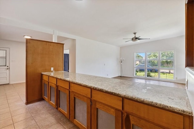 1009 Driftwood Pl, Corpus Christi, TX 78411 - kitchen with brown cabinetry, a ceiling fan, a peninsula, light tile patterned floors, and light stone countertops