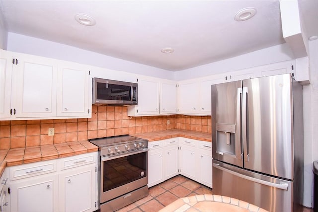 4410 Hebert, Corpus Christi, TX 78413 - kitchen featuring light tile patterned floors, white cabinets, stainless steel appliances, backsplash, and tile countertops