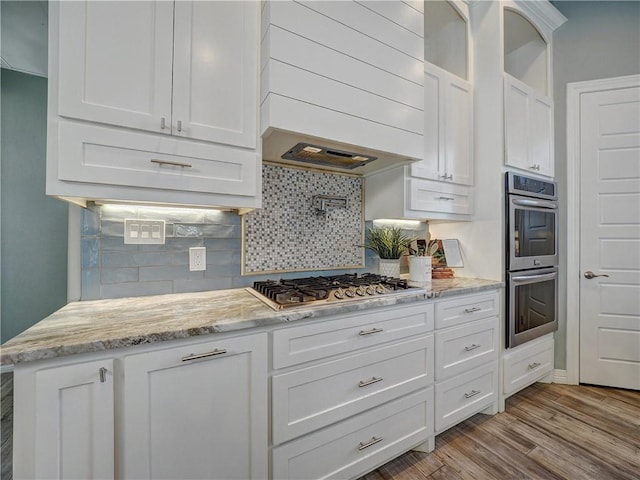 kitchen featuring appliances with stainless steel finishes, white cabinetry, wood finished floors, custom range hood, and backsplash