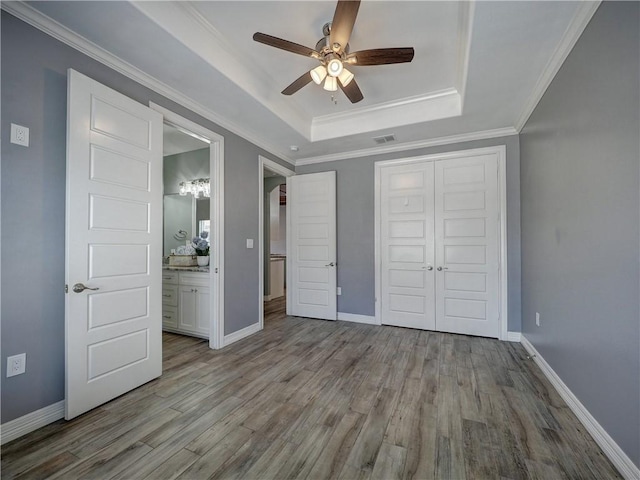 unfurnished bedroom featuring visible vents, a closet, baseboards, a raised ceiling, and wood finished floors