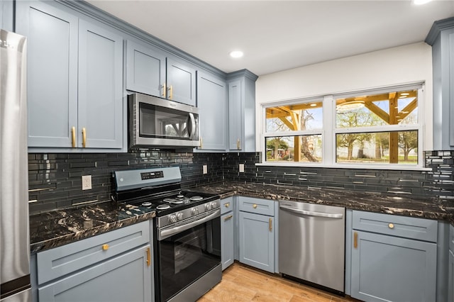 kitchen with gray cabinets, appliances with stainless steel finishes, backsplash, and dark stone counters