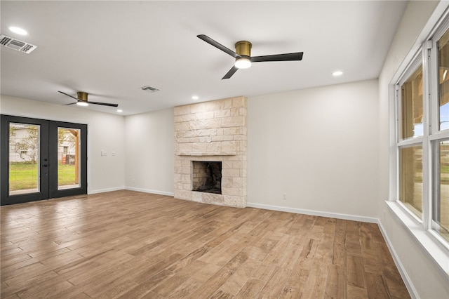 unfurnished living room featuring french doors, ceiling fan, a fireplace, and light hardwood / wood-style flooring