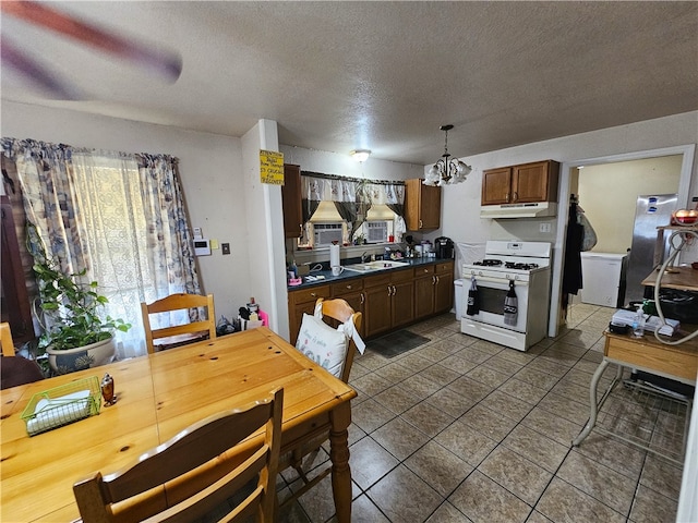 kitchen featuring white gas stove, sink, a textured ceiling, hanging light fixtures, and a chandelier