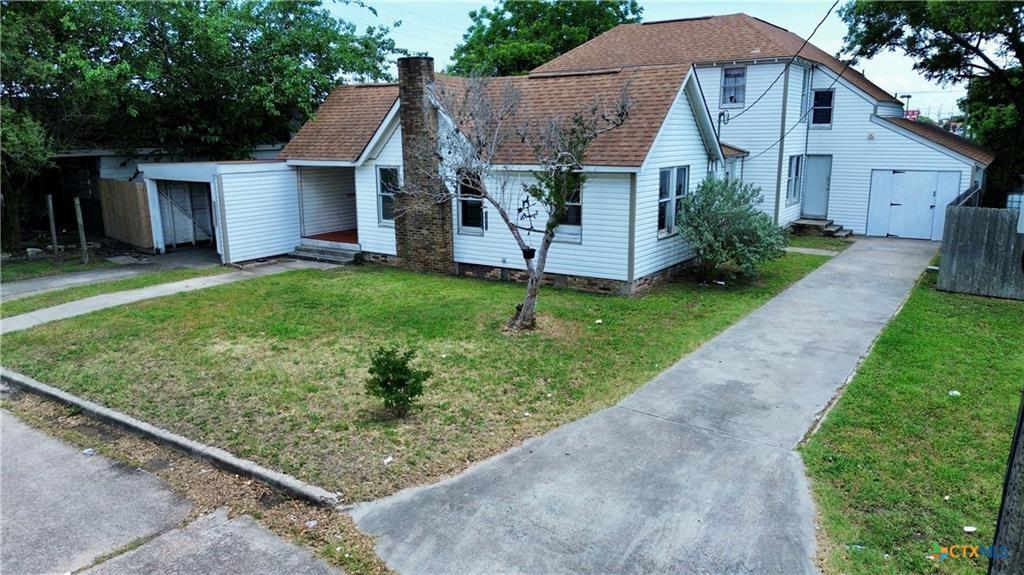 103 W Depot St, Refugio, TX 78377 - view of front of house with a chimney, a front yard, driveway, and a shingled roof