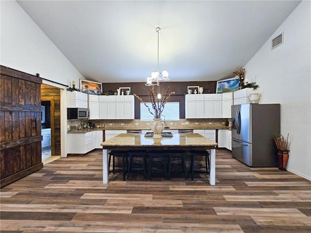 kitchen with stainless steel appliances, tasteful backsplash, white cabinets, a kitchen island, and a barn door