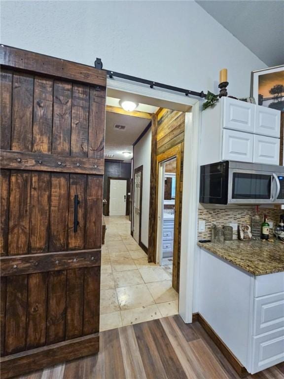 kitchen with lofted ceiling, dark stone countertops, white cabinets, decorative backsplash, and a barn door